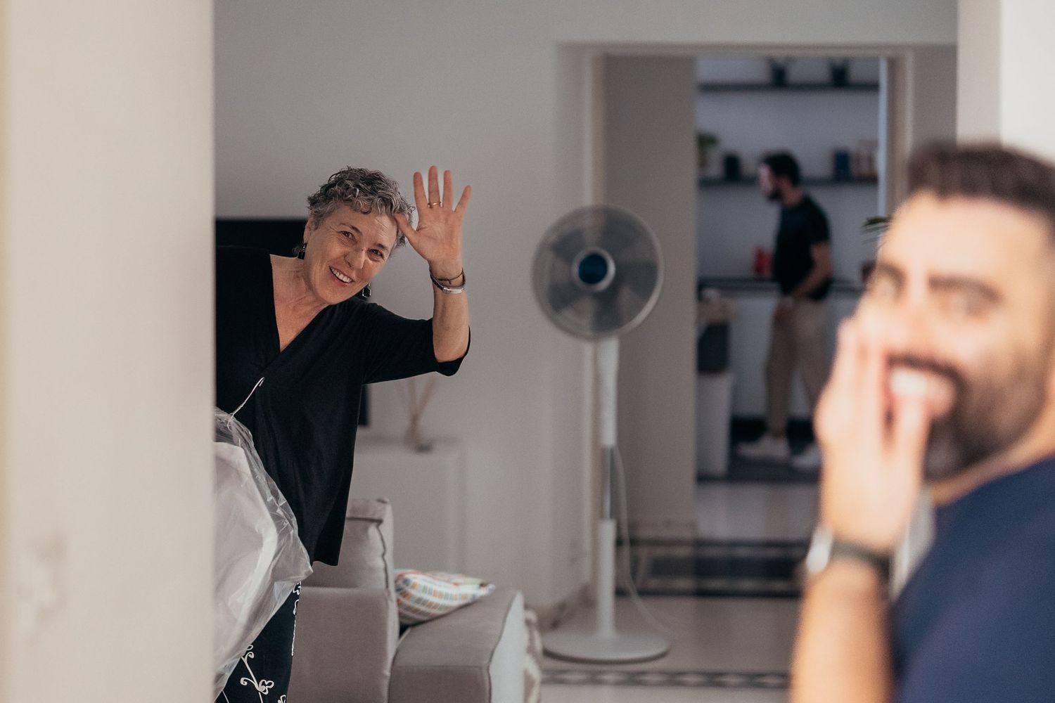 Two people interacting in a modern kitchen space with a standing fan visible in the background.