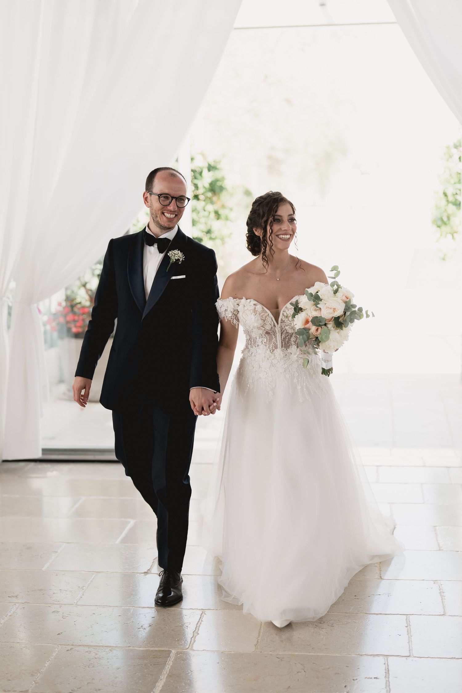 Wedding couple walking together through white draped curtains in an elegant venue.