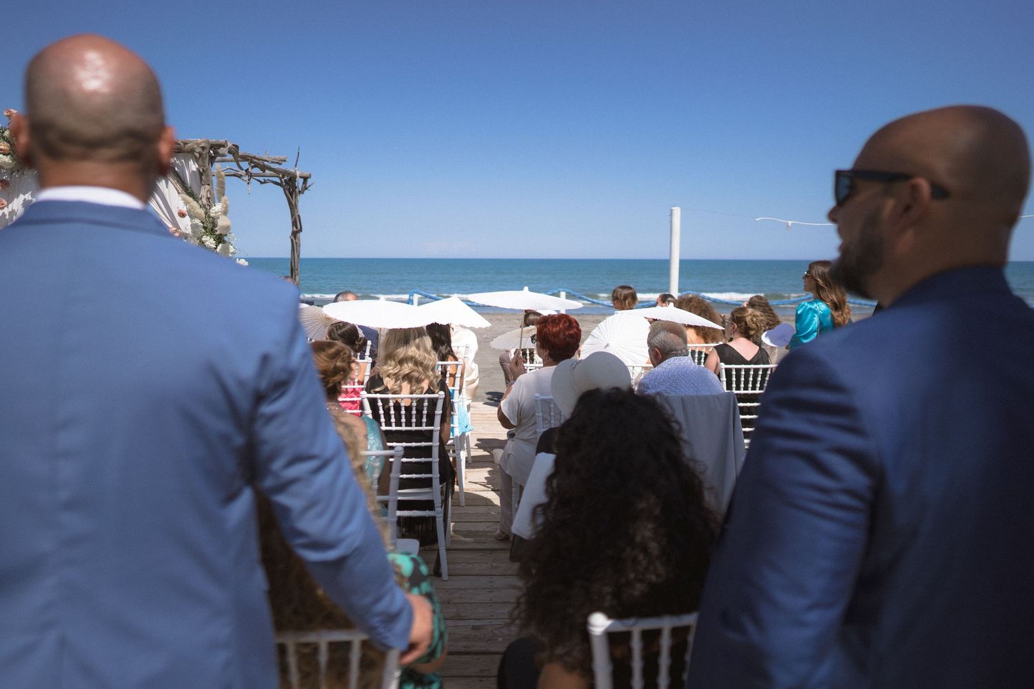 A beachside wedding ceremony setup with guests seated under blue skies.