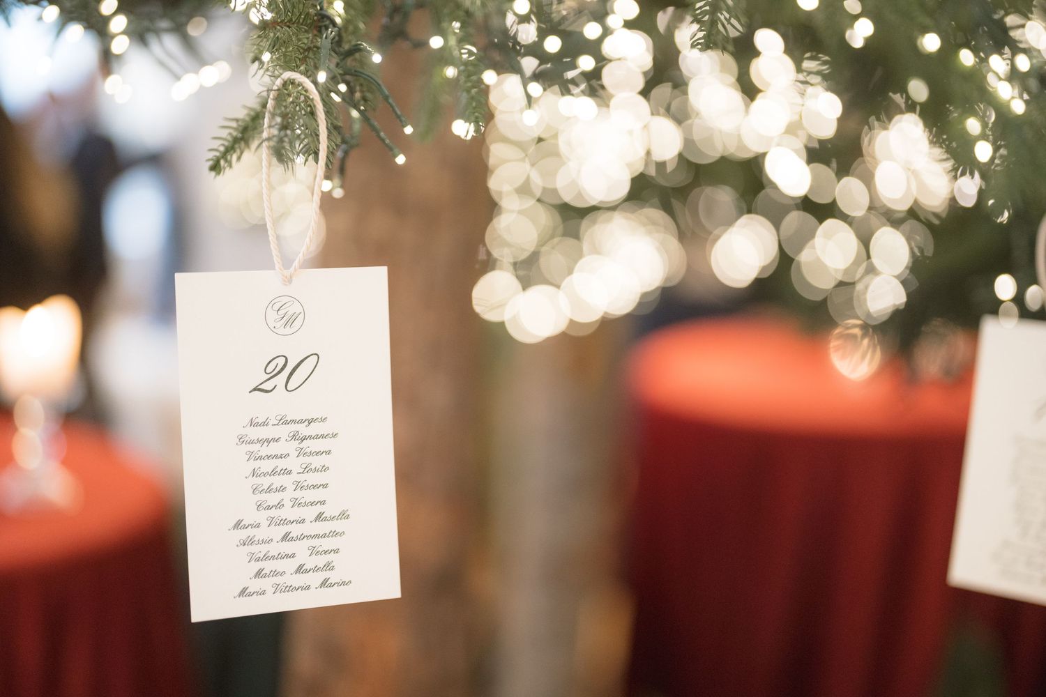 Wedding seating chart card number 20 hanging from Christmas tree with twinkling lights at festive reception.