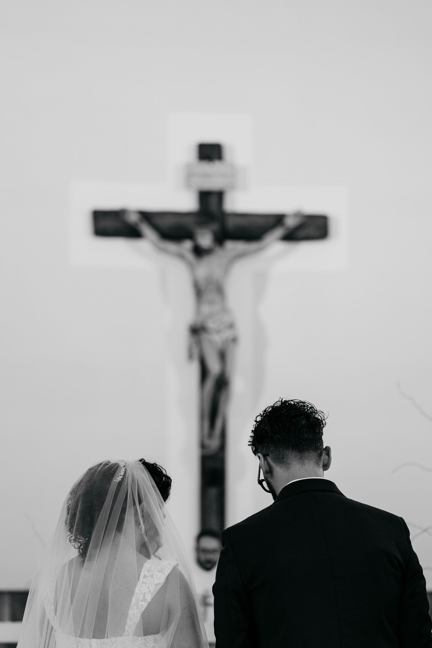 Black and white photo of bride and groom standing before a crucifix during a religious wedding ceremony.