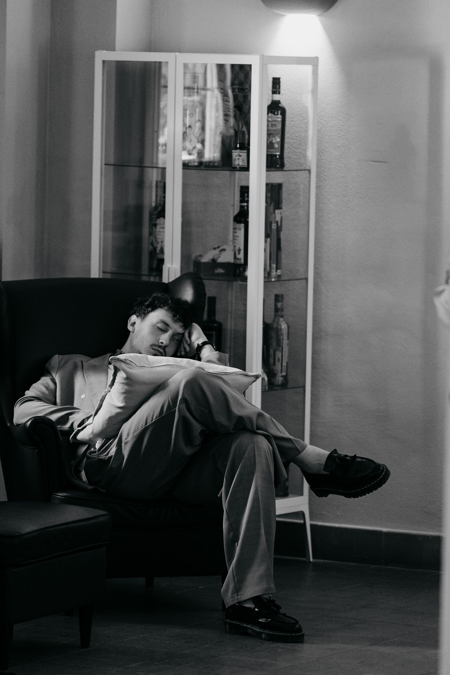 Black and white photo of a man in a suit relaxing in a chair near a liquor cabinet.