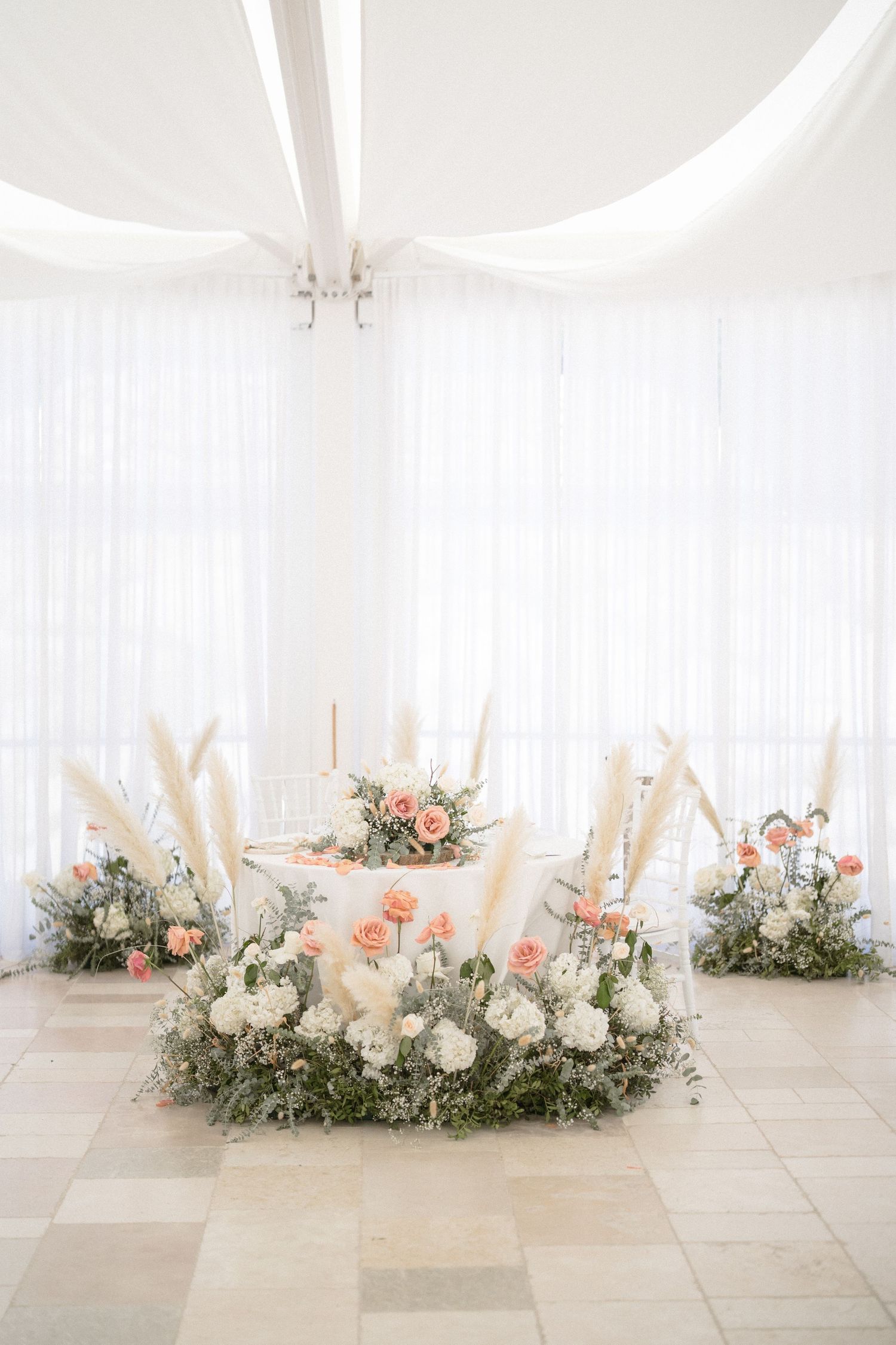 Elegant wedding reception decor featuring white and pink floral arrangements with pampas grass.