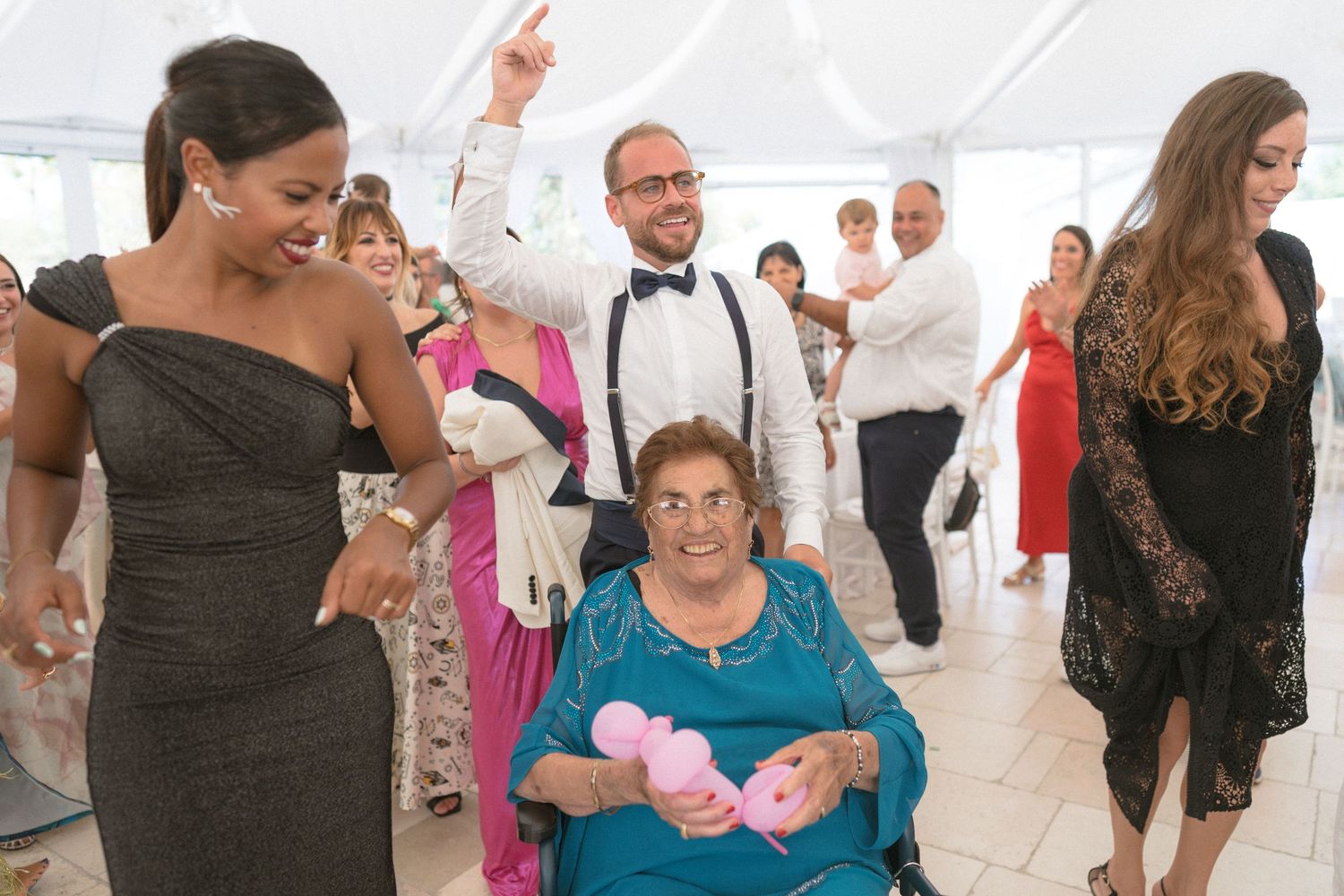 Wedding reception guests dancing and celebrating in a white tent venue.