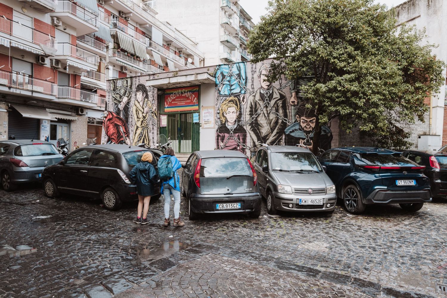 Urban street corner with parked cars and apartment buildings in Naples, Italy.