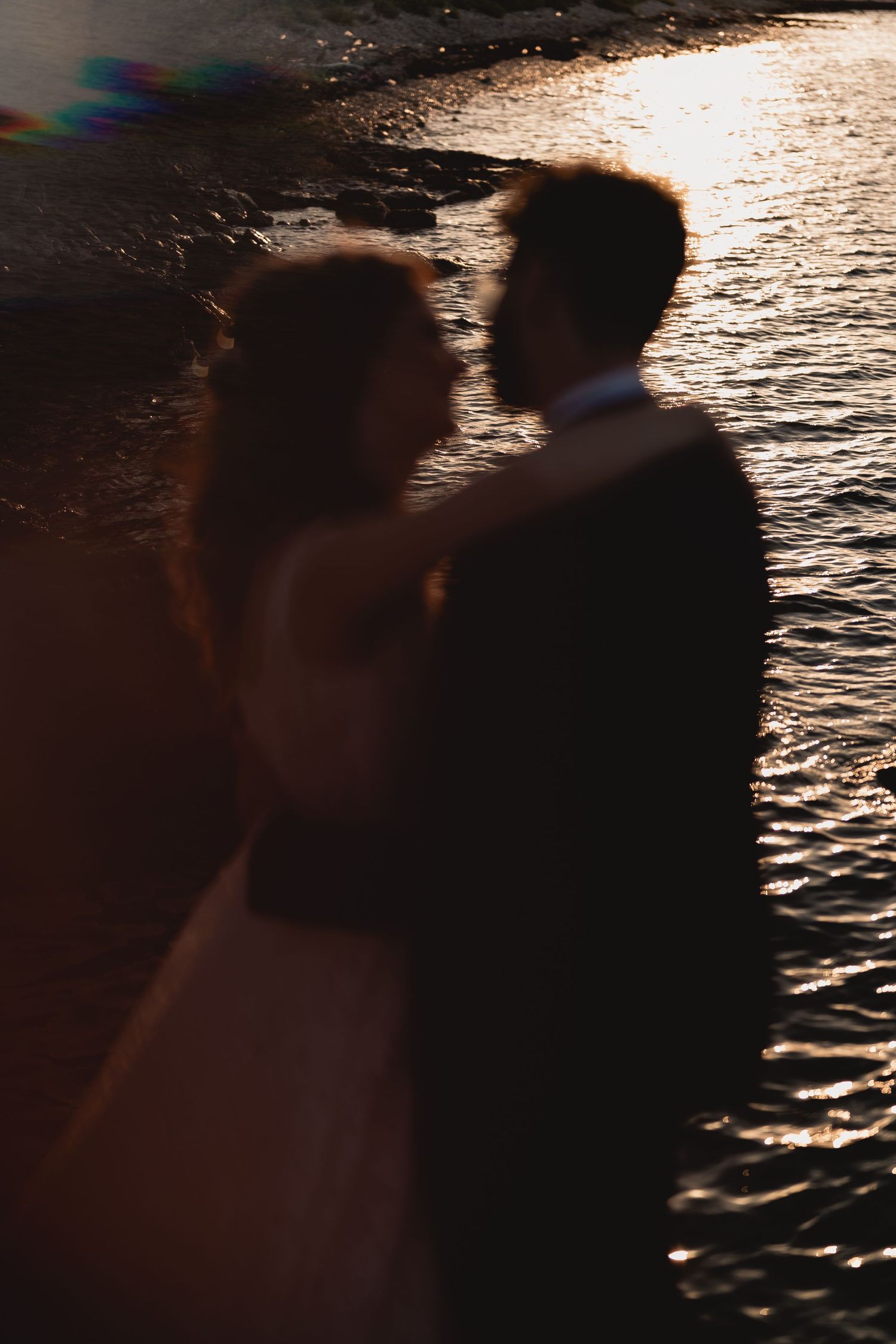 Backlit silhouette of newlyweds by the ocean during sunset.