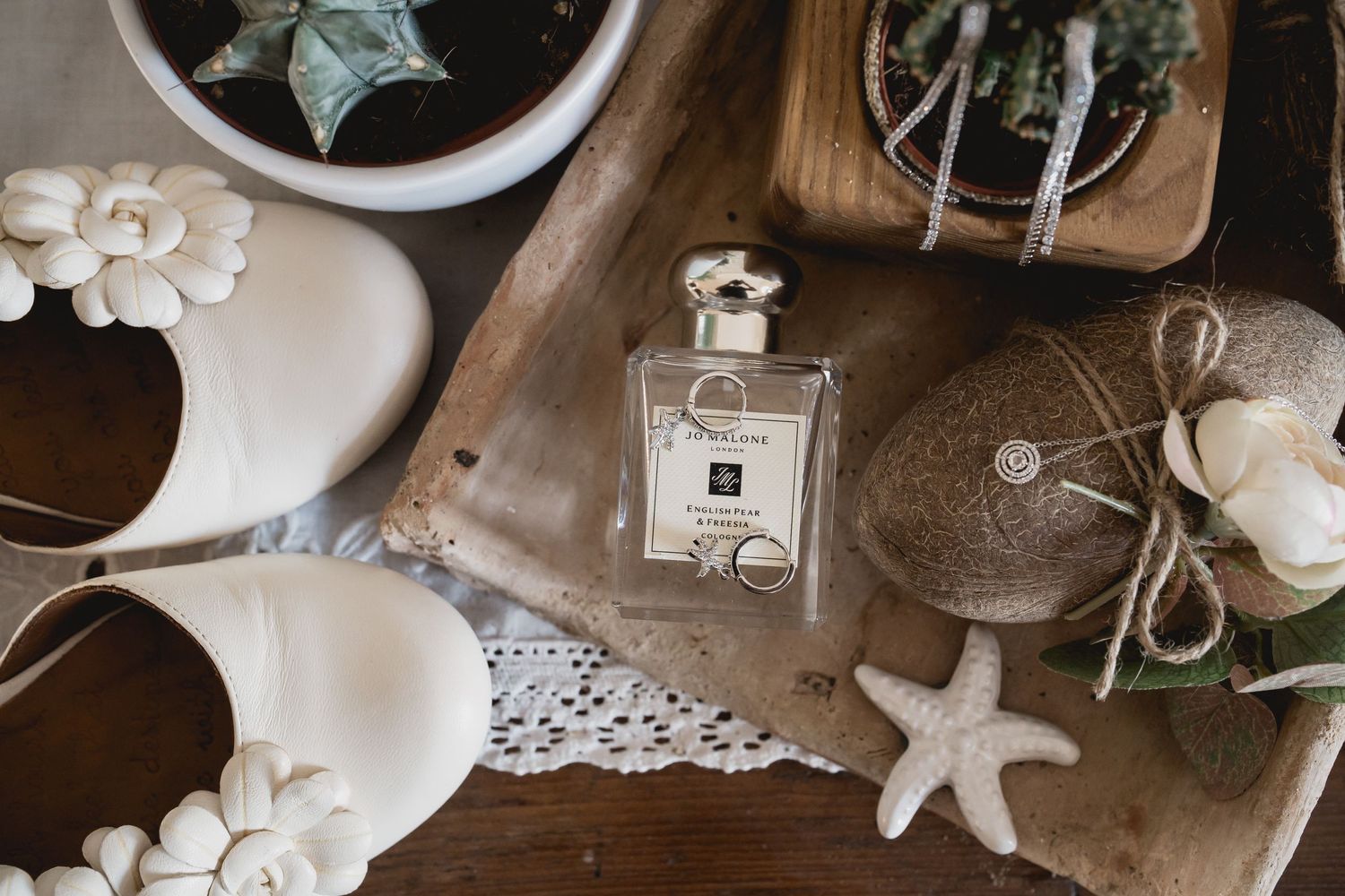 Flat lay of perfume bottle, starfish, and white flowers on rustic wooden surface with lace doily.