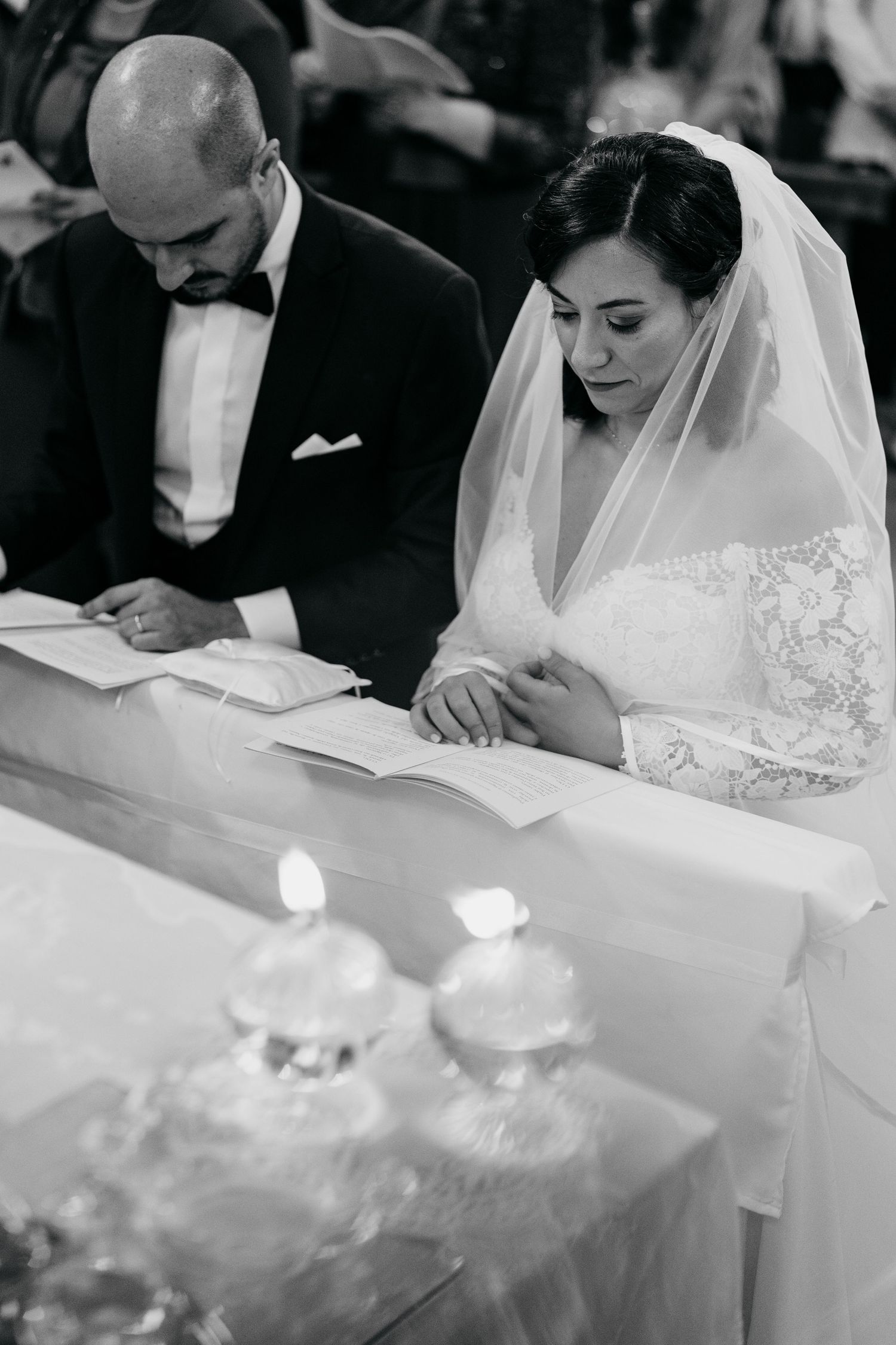 Black and white photo of couple signing documents during wedding ceremony with candles.