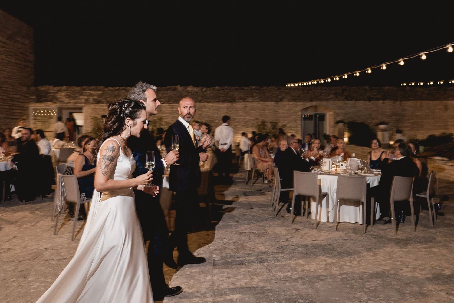 Wedding reception at night with string lights and guests seated at tables.