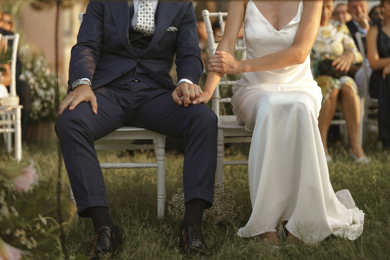 Close-up shot of newlyweds sitting together outdoors with groom in navy suit and bride in flowing white gown.