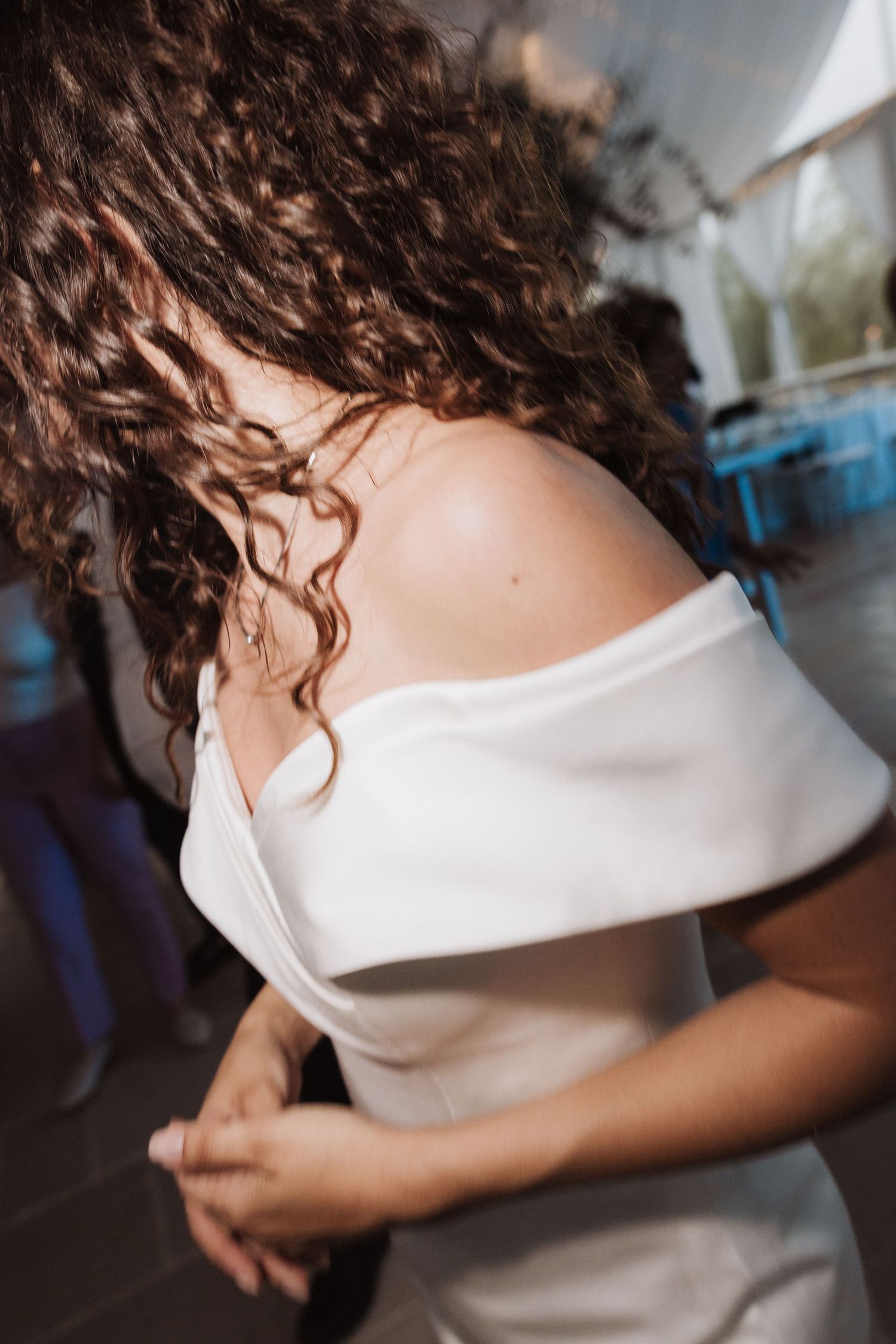 Detail shot of white off-shoulder wedding dress and natural curly hair.