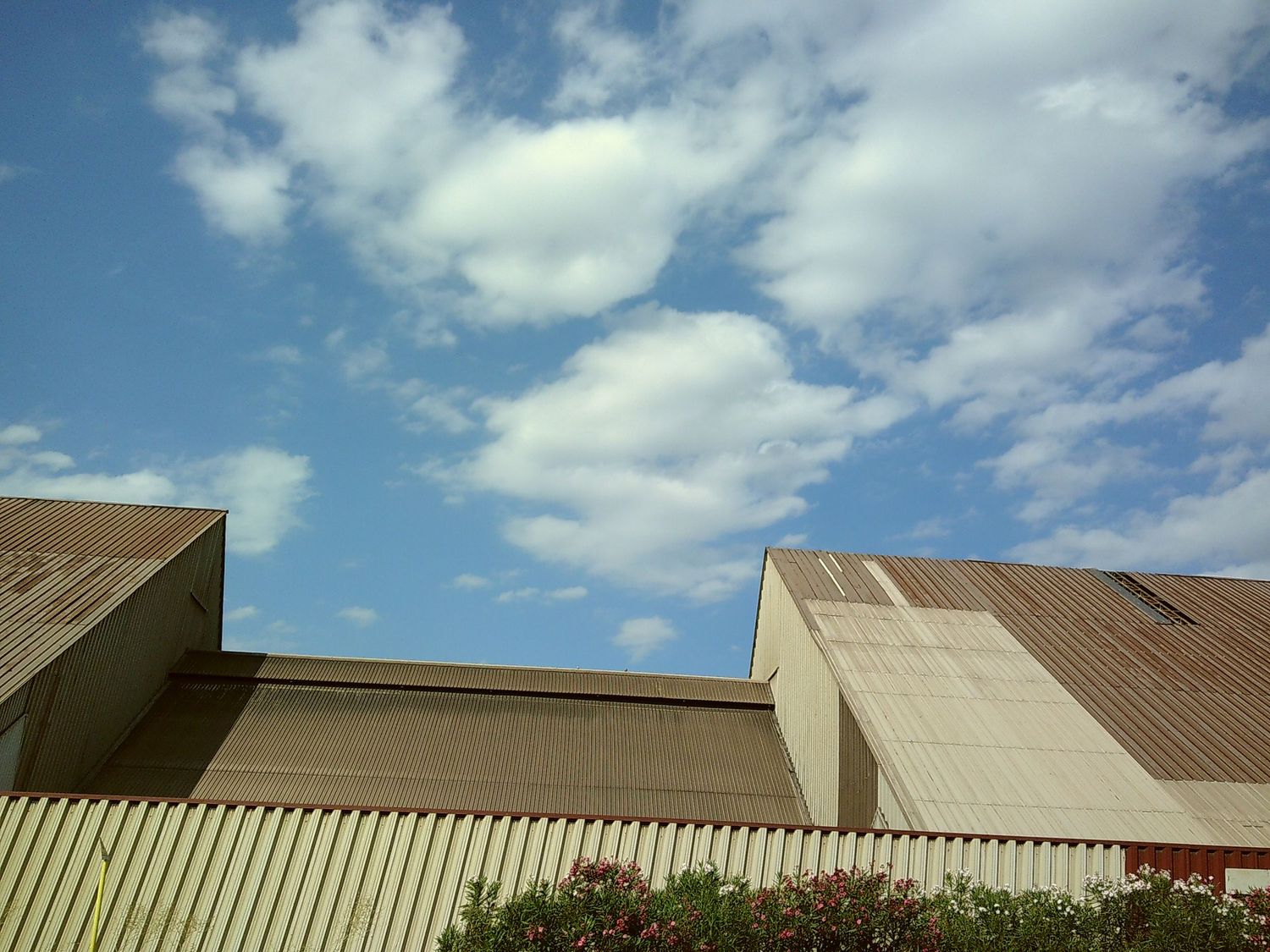 Modern industrial building with angular architecture against a bright blue sky with white clouds.