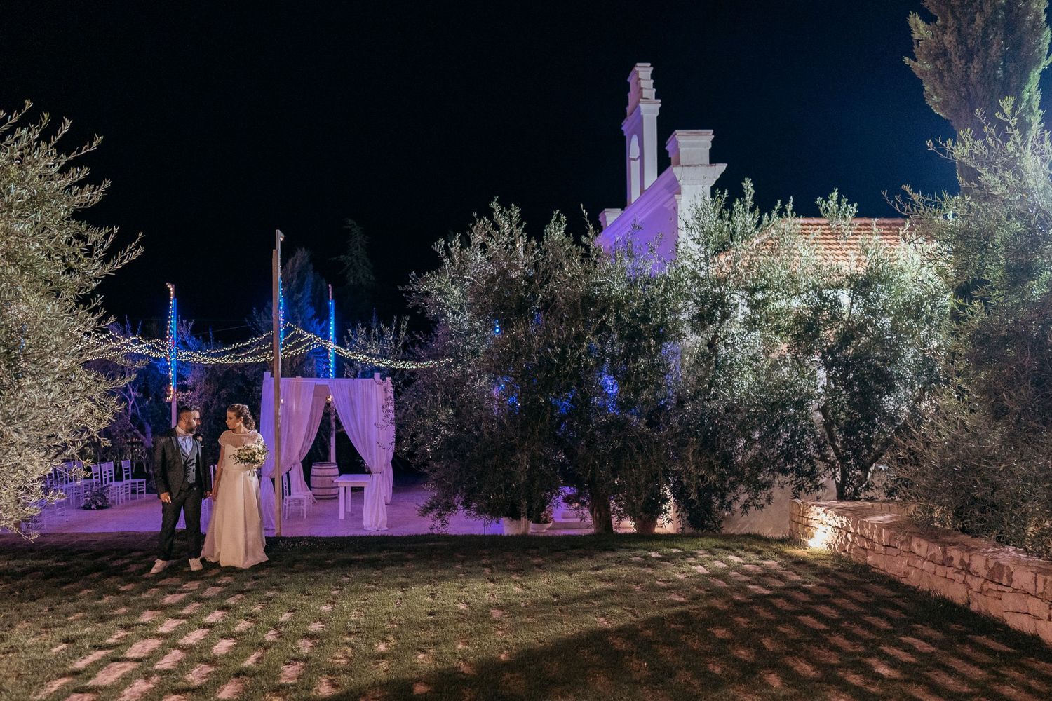 Outdoor wedding venue illuminated with purple and blue lights at night.