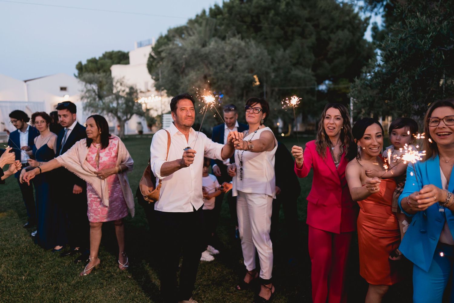 Wedding guests holding sparklers during evening celebration outdoors.