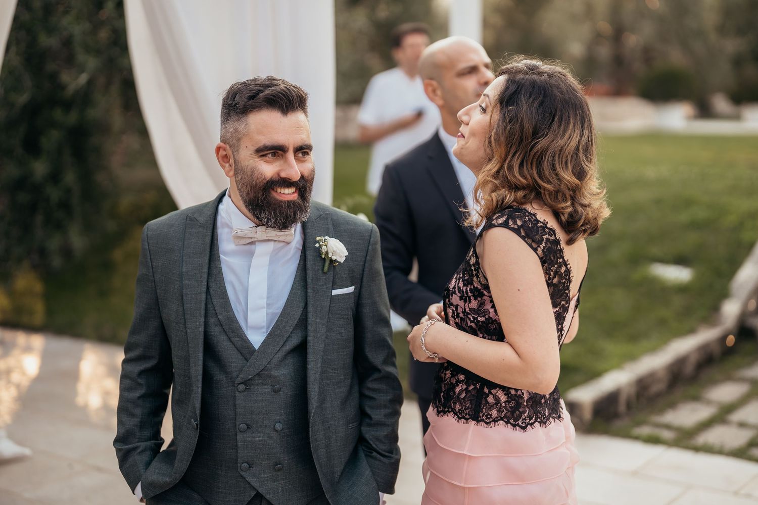 Elegant wedding party gathering outdoors with formal attire and decorative white drapes.