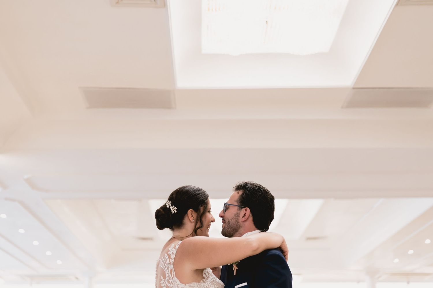 A couple shares an intimate dance at their wedding reception in an elegant white ballroom.