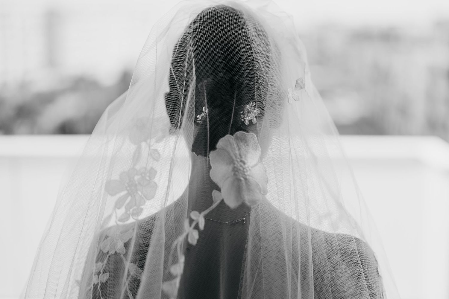 A close-up artistic shot of a bride wearing a delicate veil in black and white.