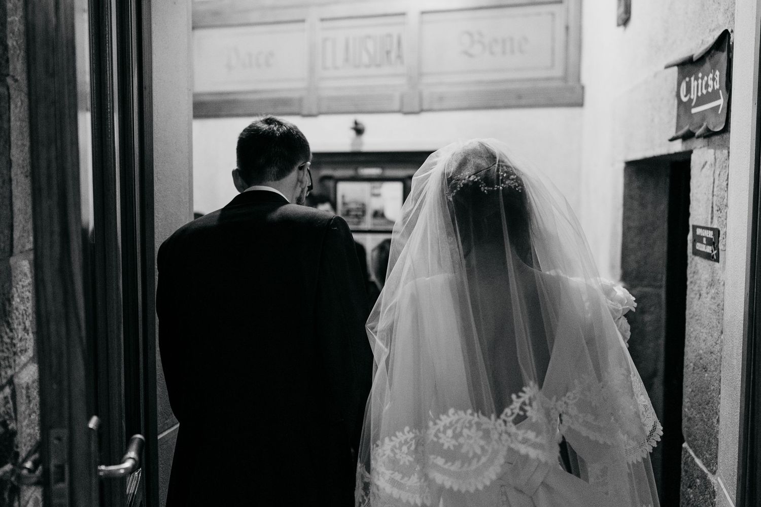Black and white rear view of a bride and groom entering a historic church doorway on their wedding day.