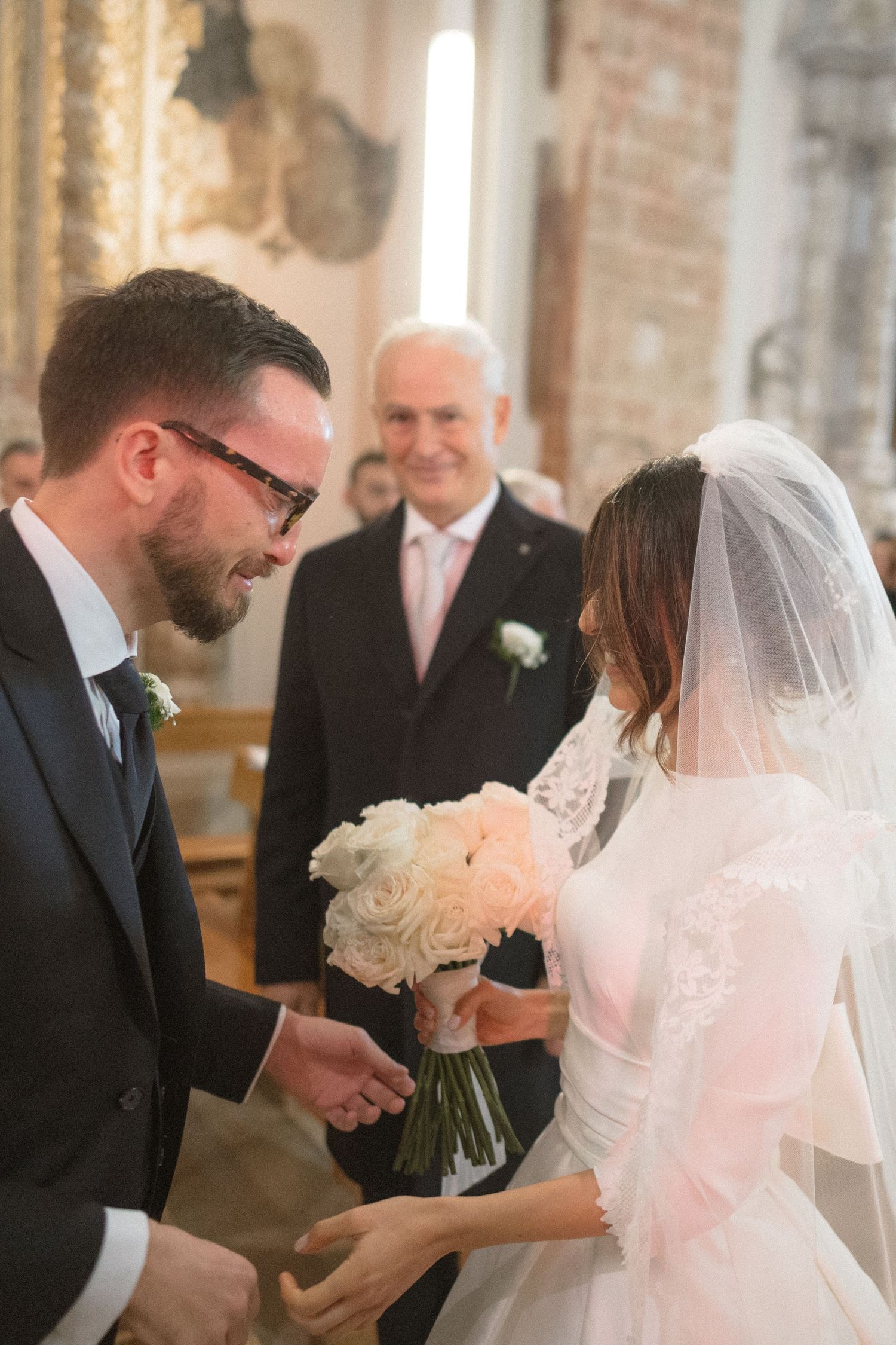 Groom in dark suit takes bride's hand at church altar during wedding ceremony.