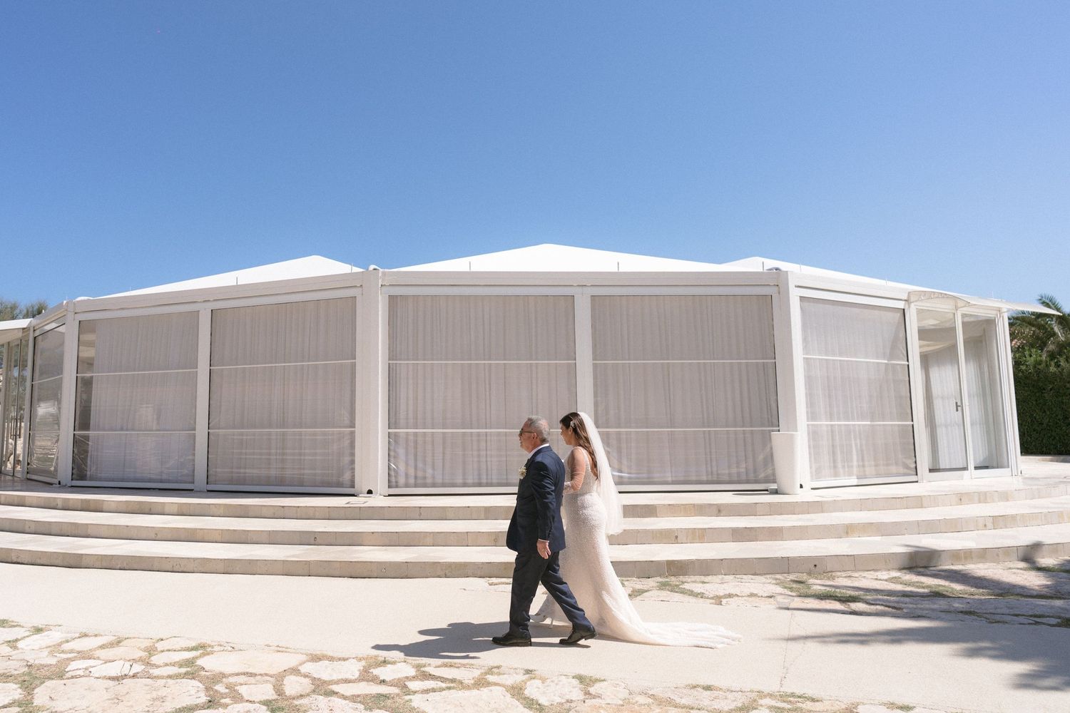 Outdoor wedding venue with white tent structures and steps under bright blue sky.