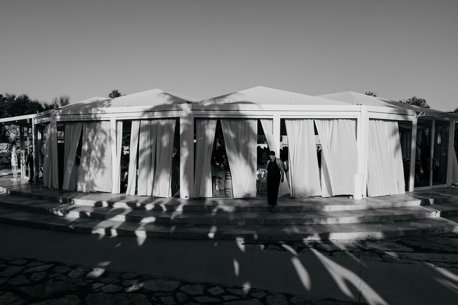 Black and white photo of a modern white tent structure with draped fabric walls.