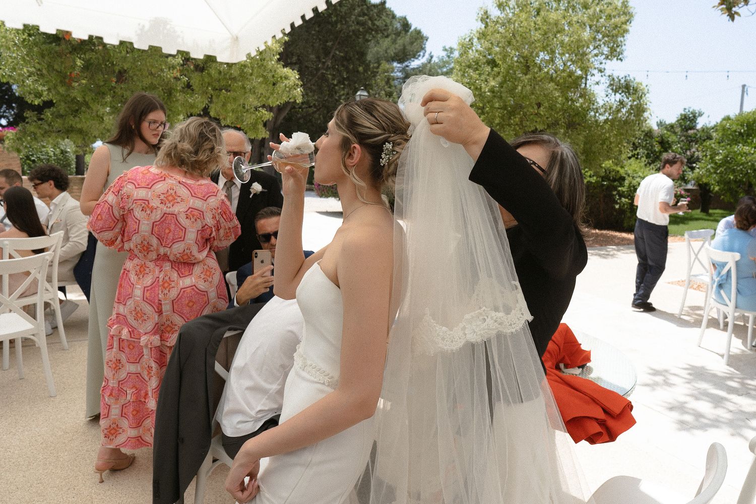 A wedding celebration outdoors with guests gathered around as a couple shares a tender moment under a veil.