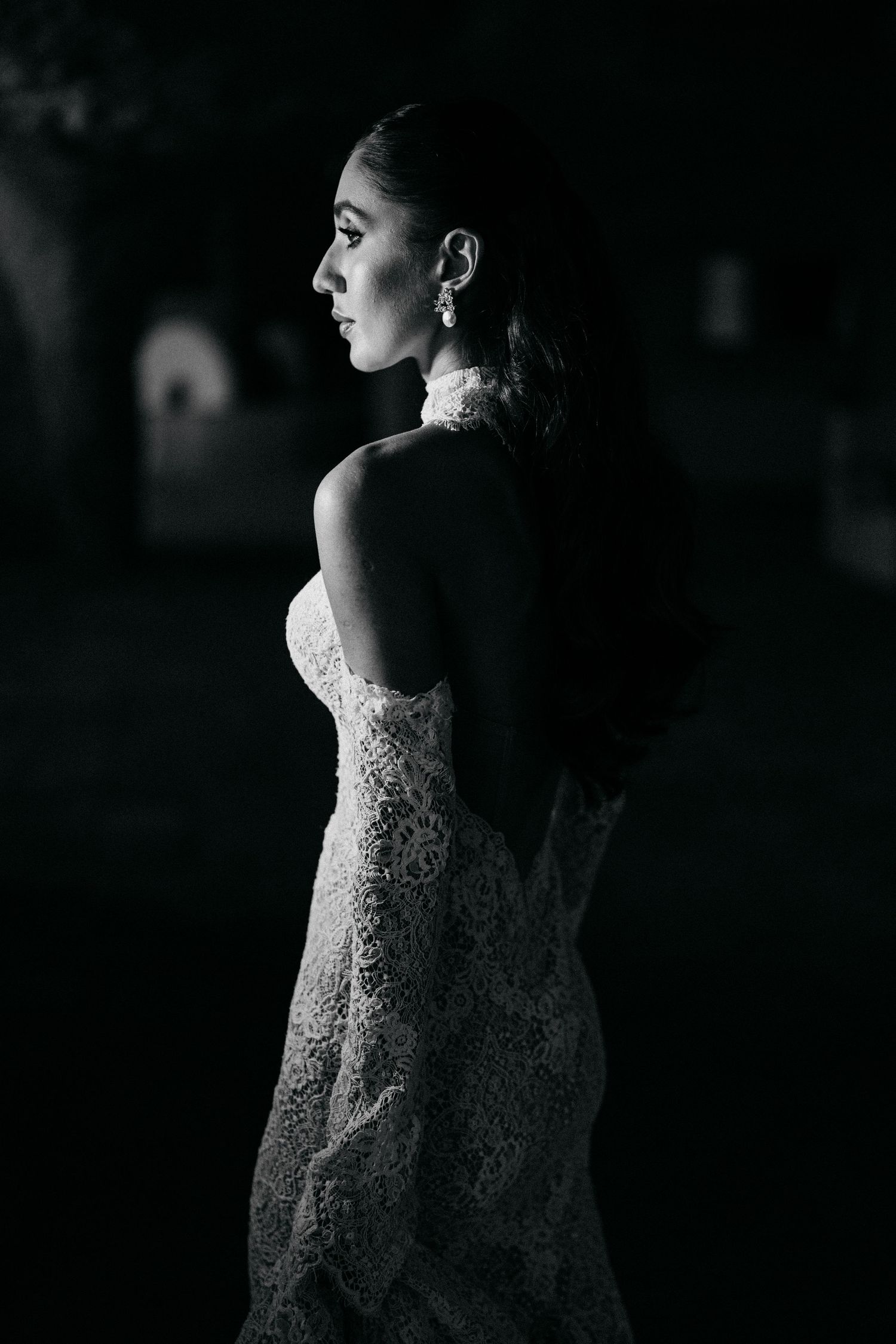 Black and white side profile of a bride in an elegant lace wedding gown with a high collar and drop earrings.