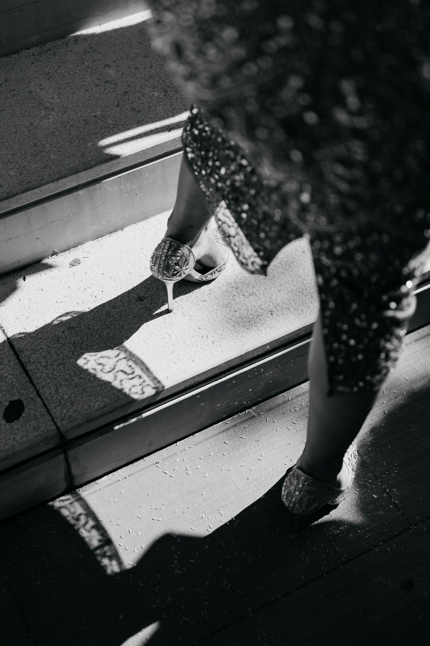 Black and white overhead shot of woman in patterned dress holding wine glass on sunny steps.