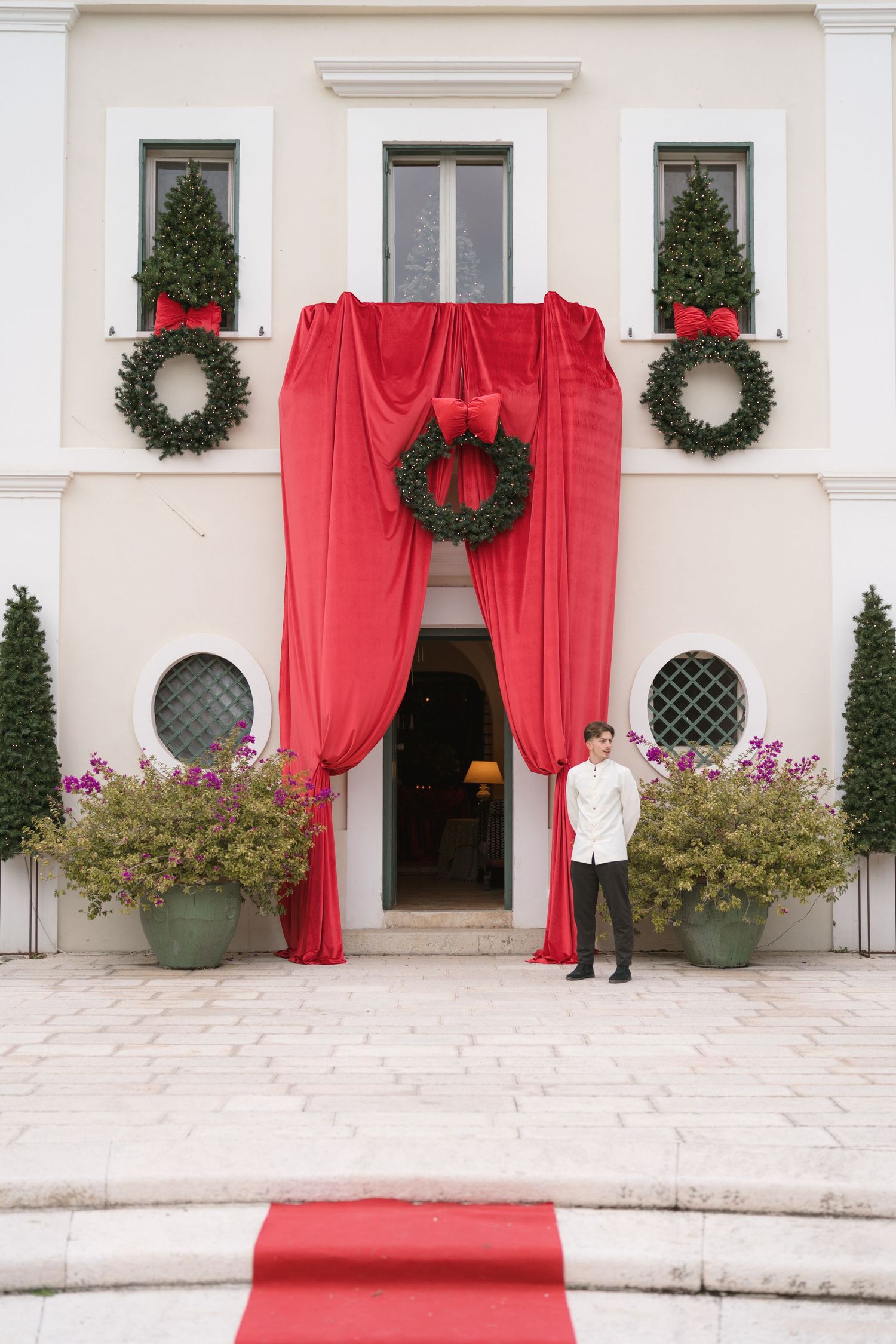 Elegant hotel entrance decorated with red drapes, Christmas wreaths, and a red carpet, with a doorman standing outside.