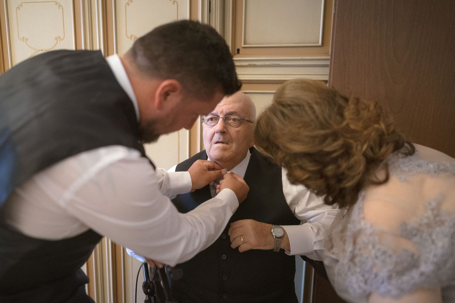 A wedding party helps adjust a tie and boutonniere during formal preparations in an elegant room.