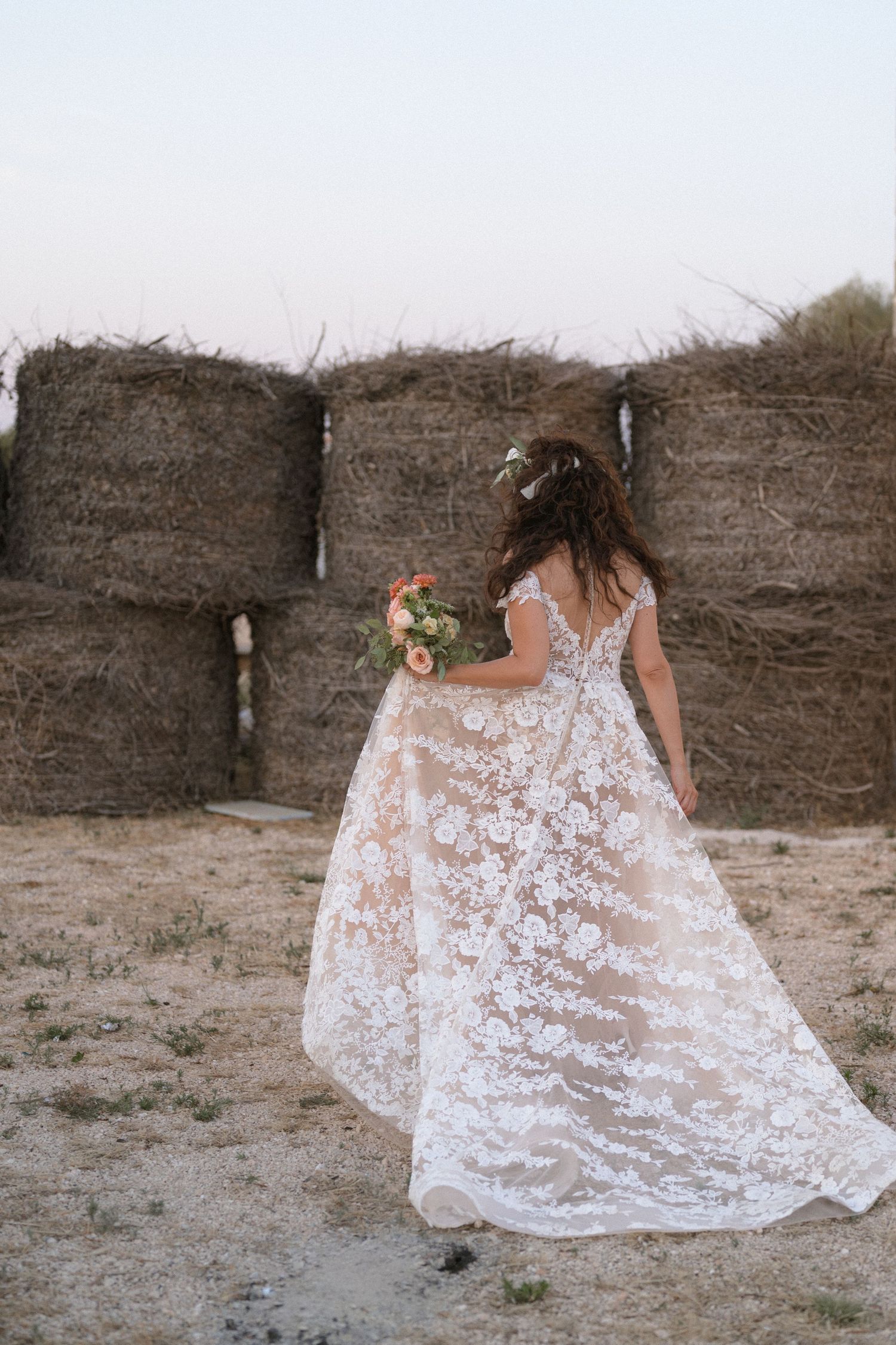 Flowing white lace wedding dress photographed against rustic hay bales in a series of artistic shots.