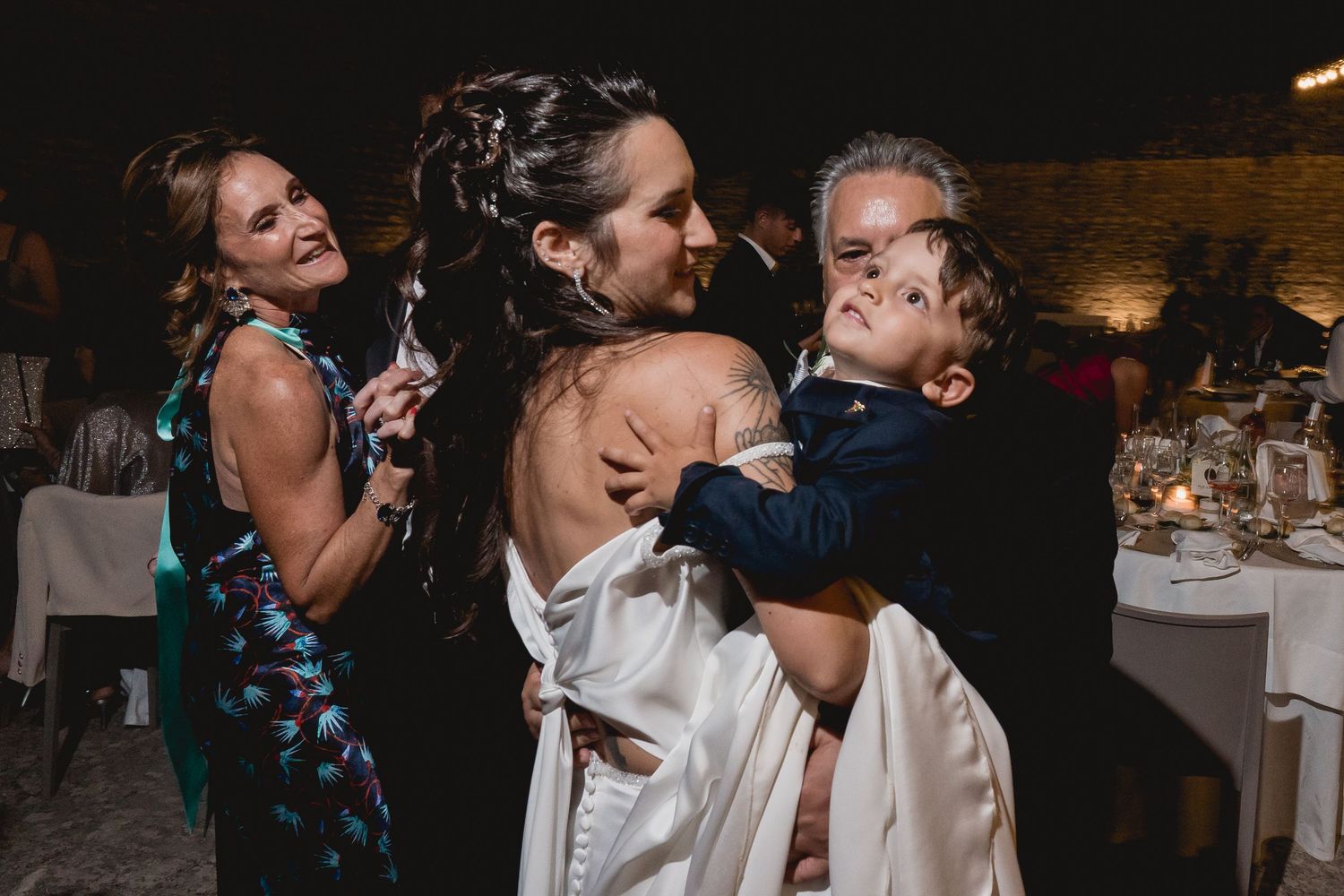 A joyful candid moment captured during a wedding reception with guests smiling and embracing.