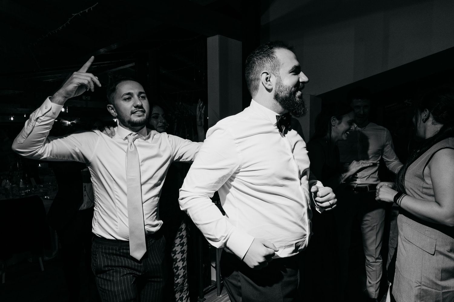 Black and white photo of guests dancing and celebrating at a wedding reception.