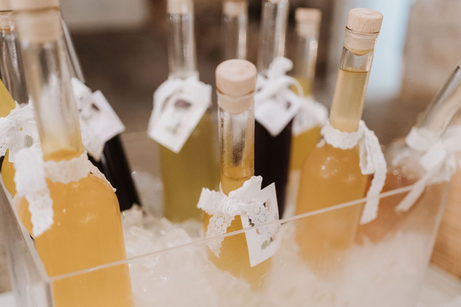 Decorative glass bottles of yellow cocktails with white tags arranged for a wedding celebration.