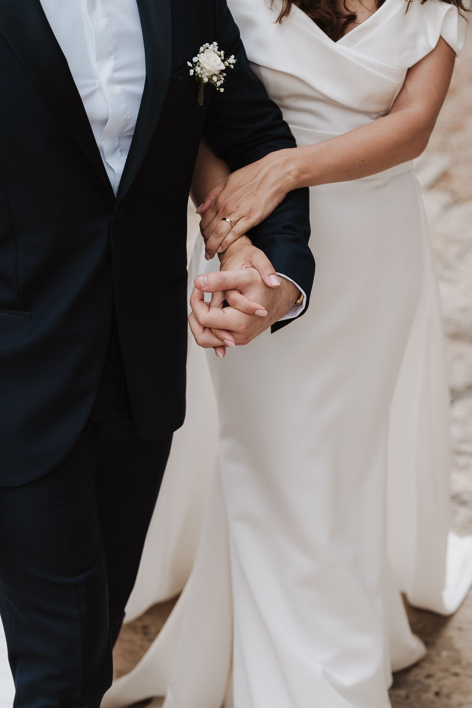 Close up of clasped hands showing wedding rings against formal wedding attire.