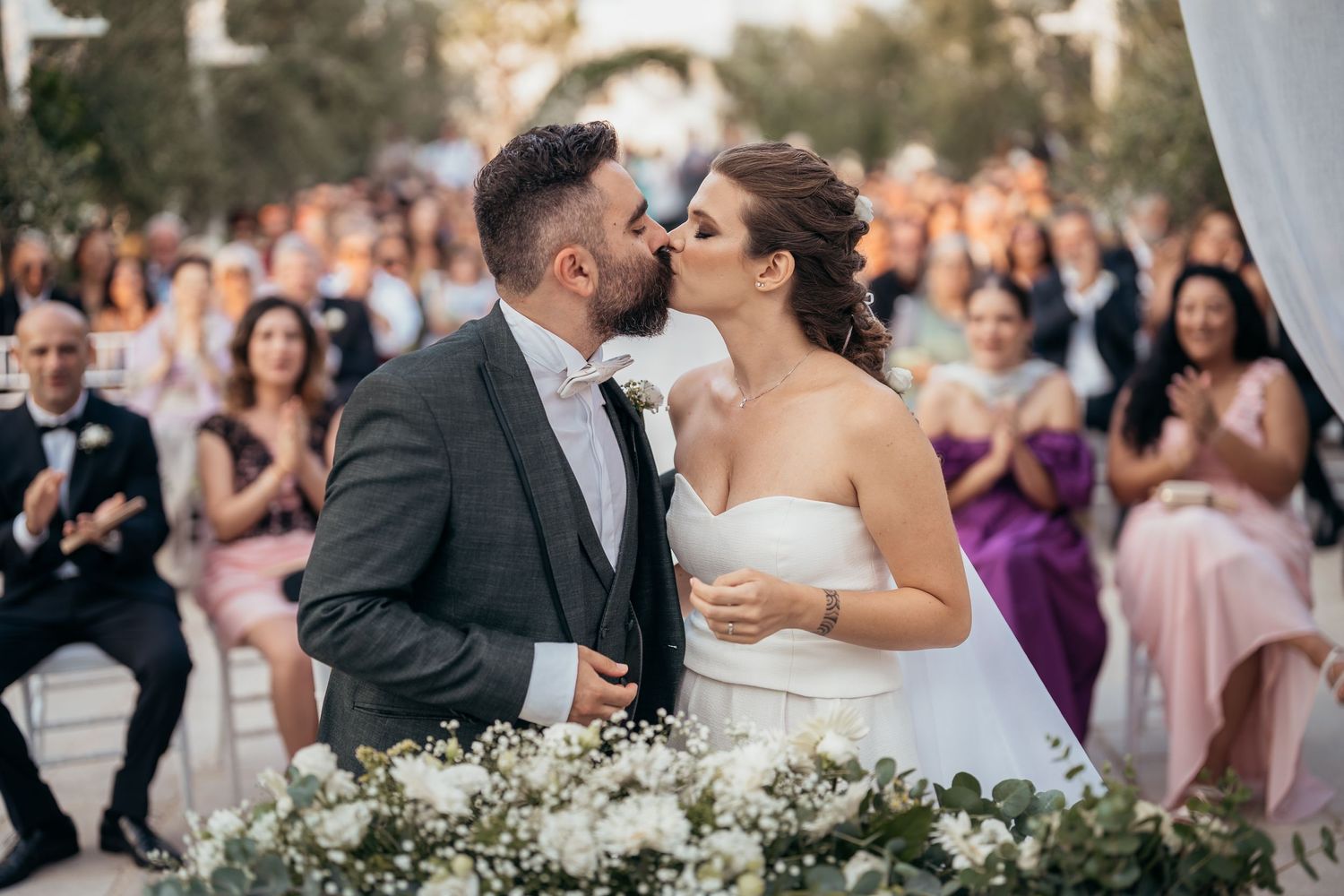 Romantic wedding moment with couple surrounded by floral arrangements and guests.