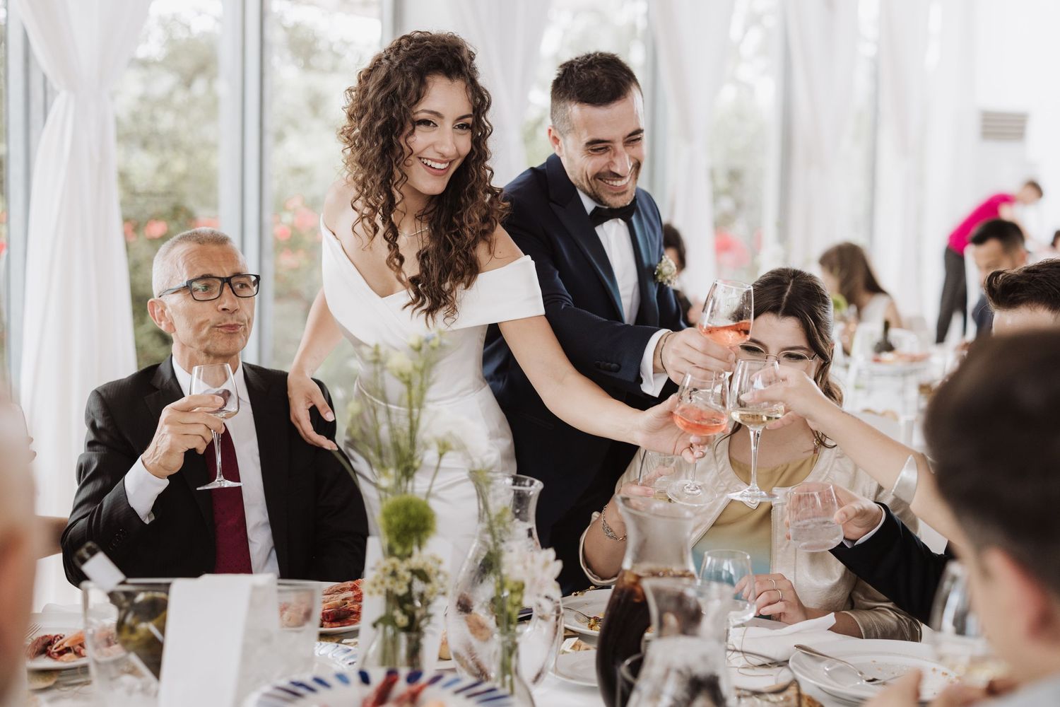 Wedding celebration with guests toasting at an elegant white-draped reception venue.