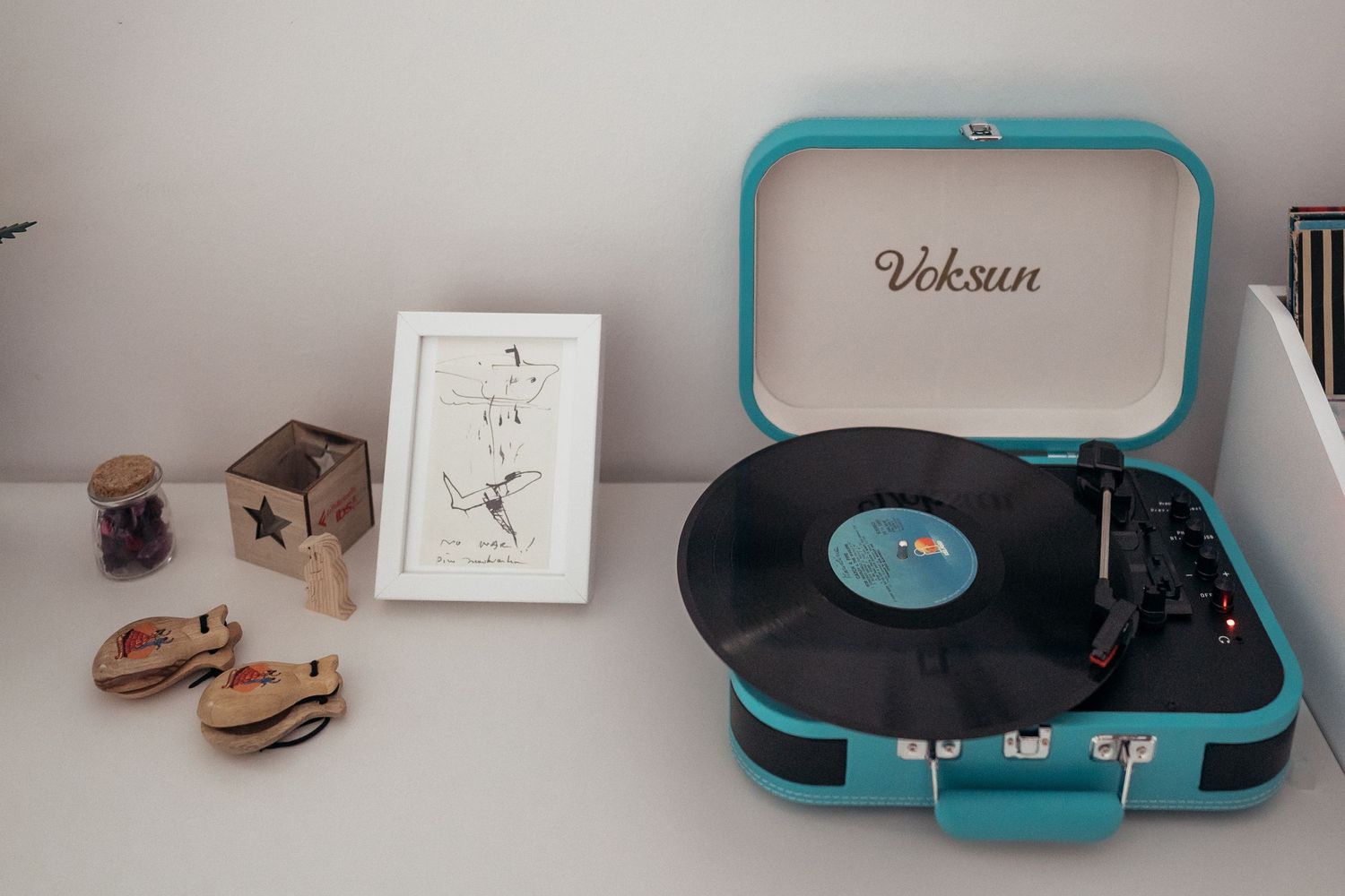 A turquoise vintage record player sits on a white surface with decorative items.