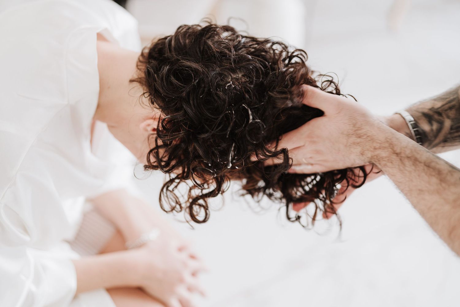 Close-up of hands styling curly dark hair against a white background.