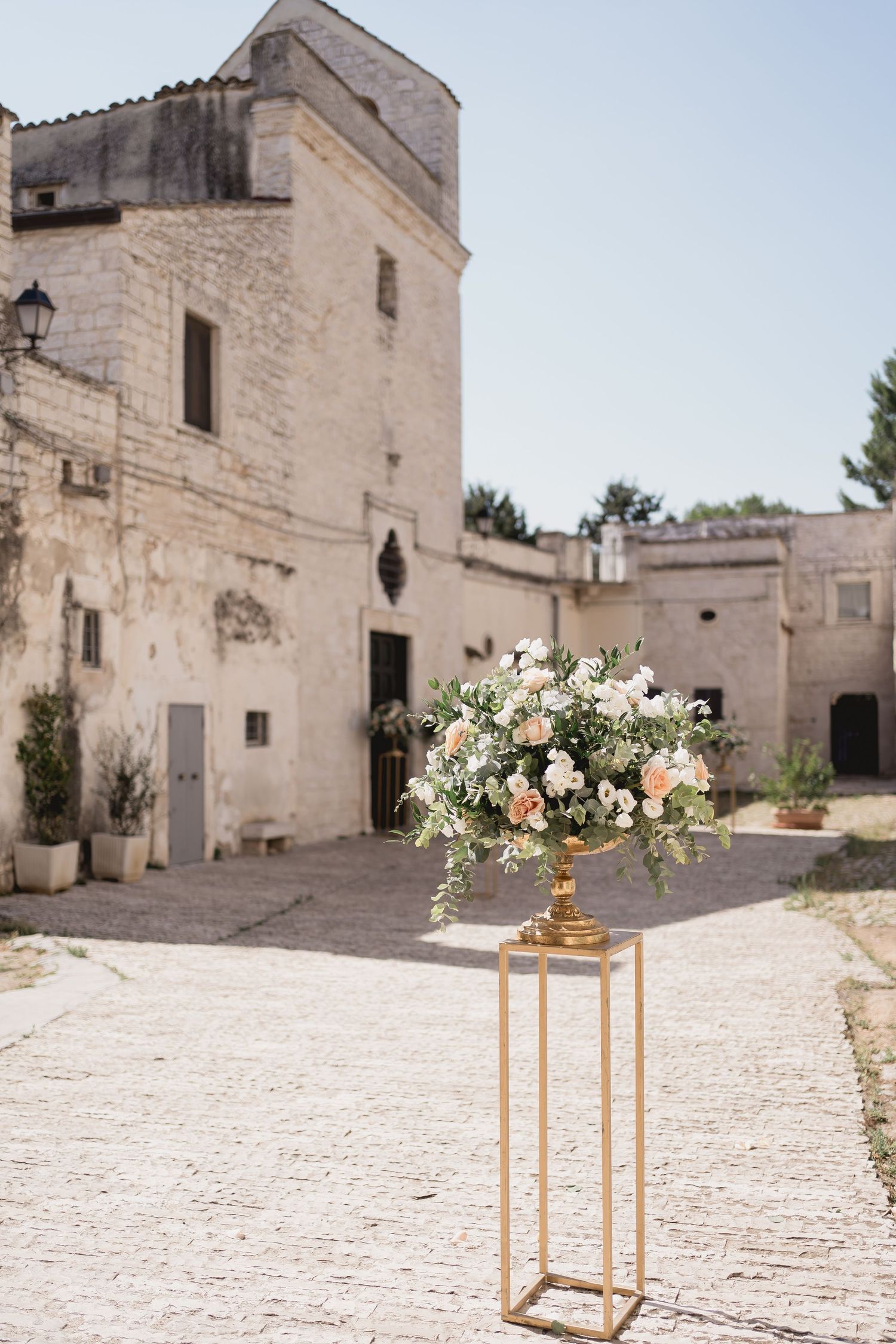 Elegant floral arrangement on gold stand outside historic stone building in natural daylight.