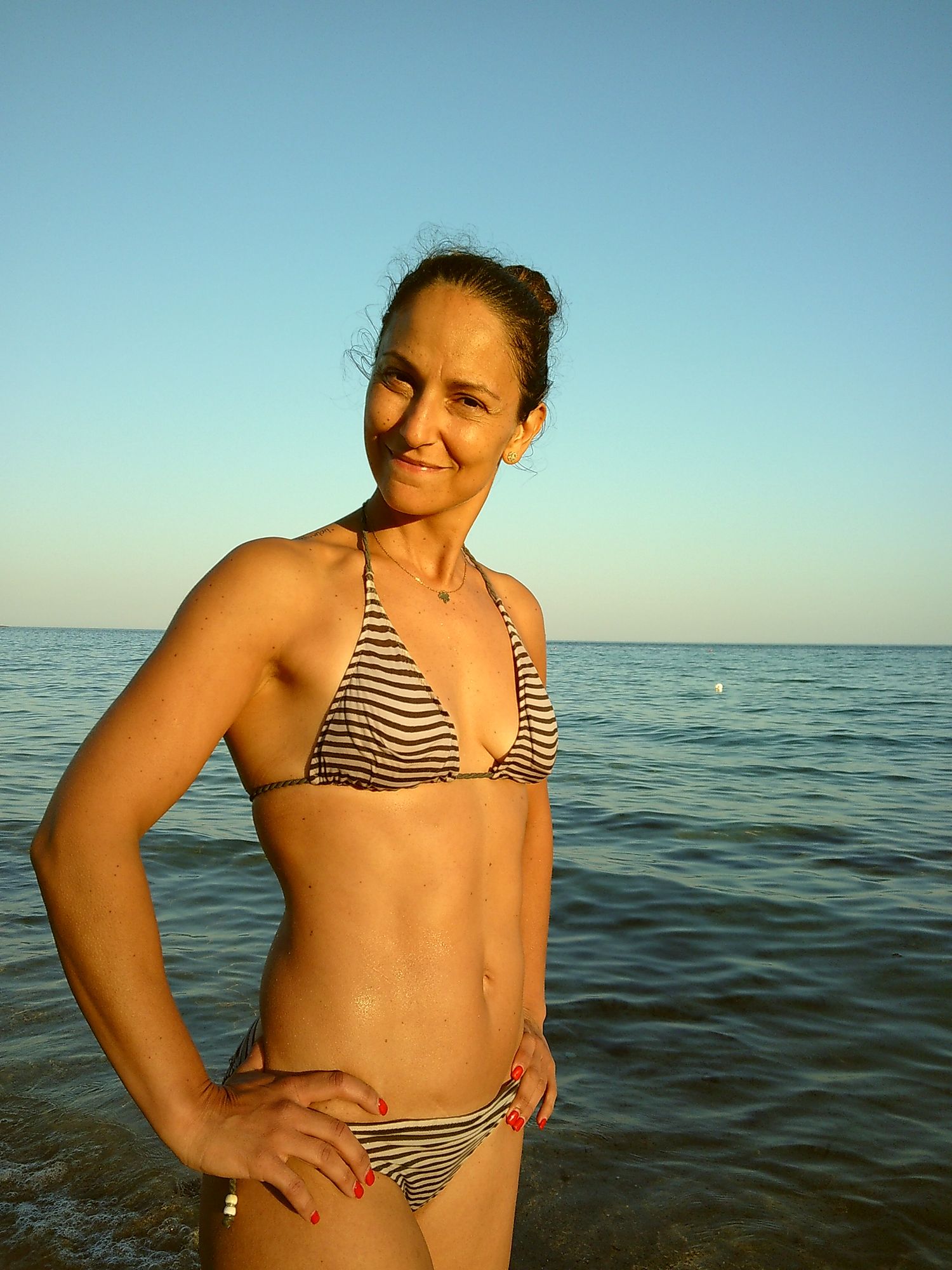 Woman in striped bikini poses at the beach with ocean waves in background.