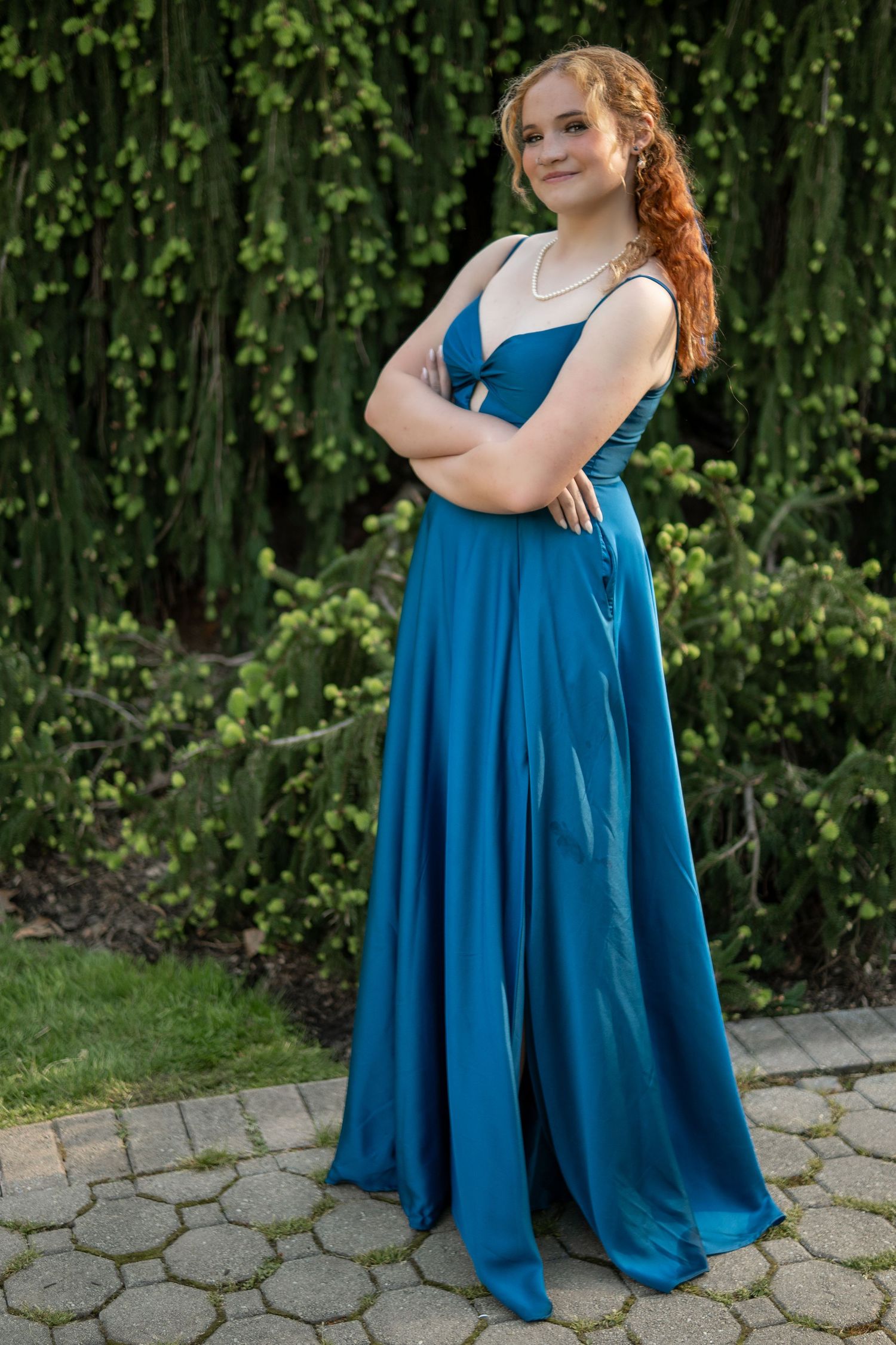 Elegant blue formal dress photographed against lush green foliage and stone pathway.