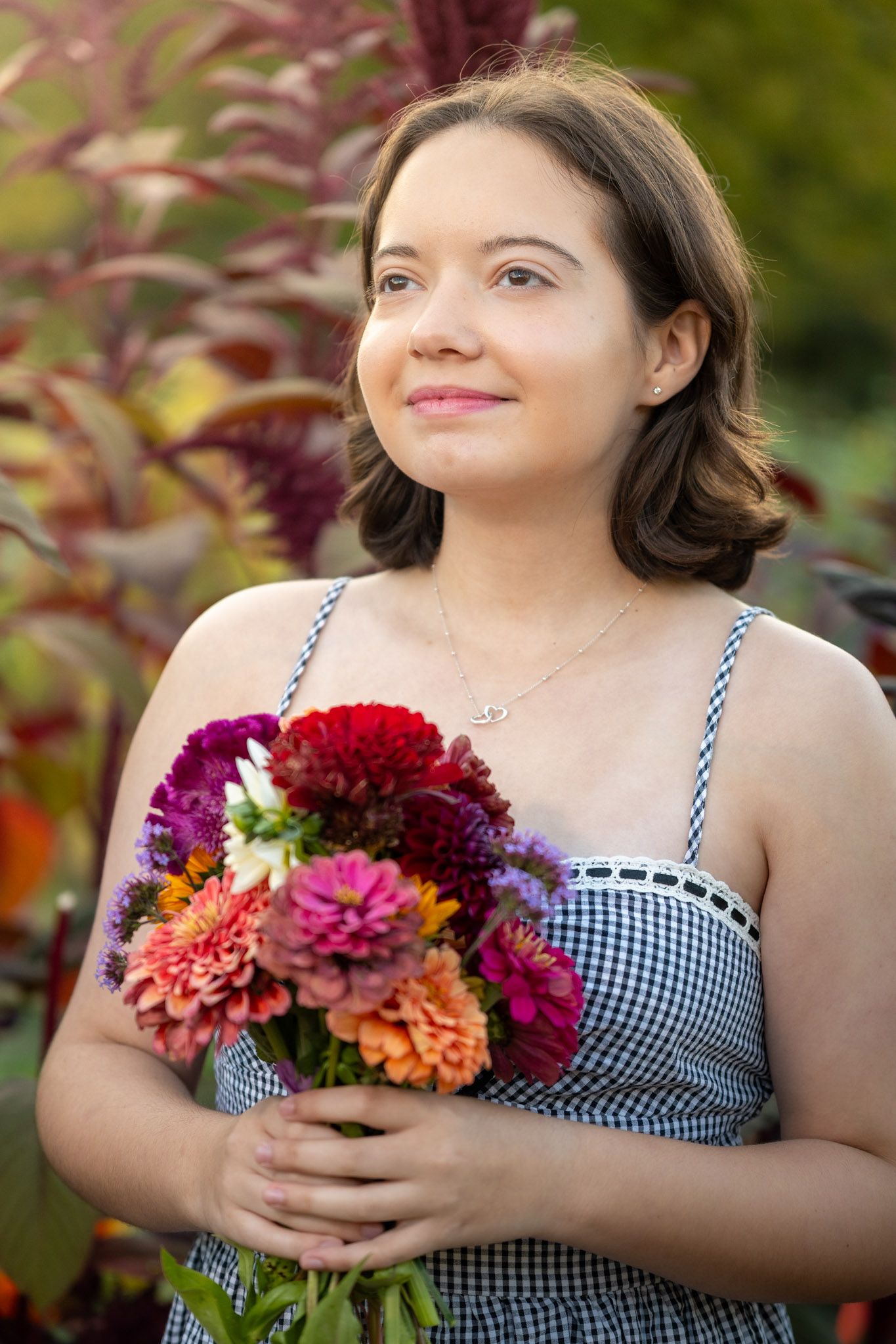 Person in gingham dress holding colorful bouquet of dahlias and flowers.