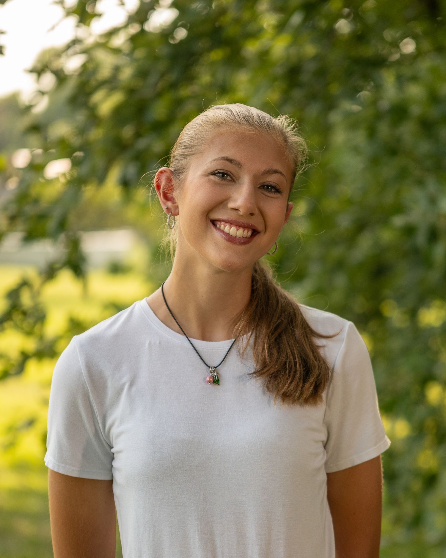A person in a white t-shirt smiles outdoors during golden hour lighting.