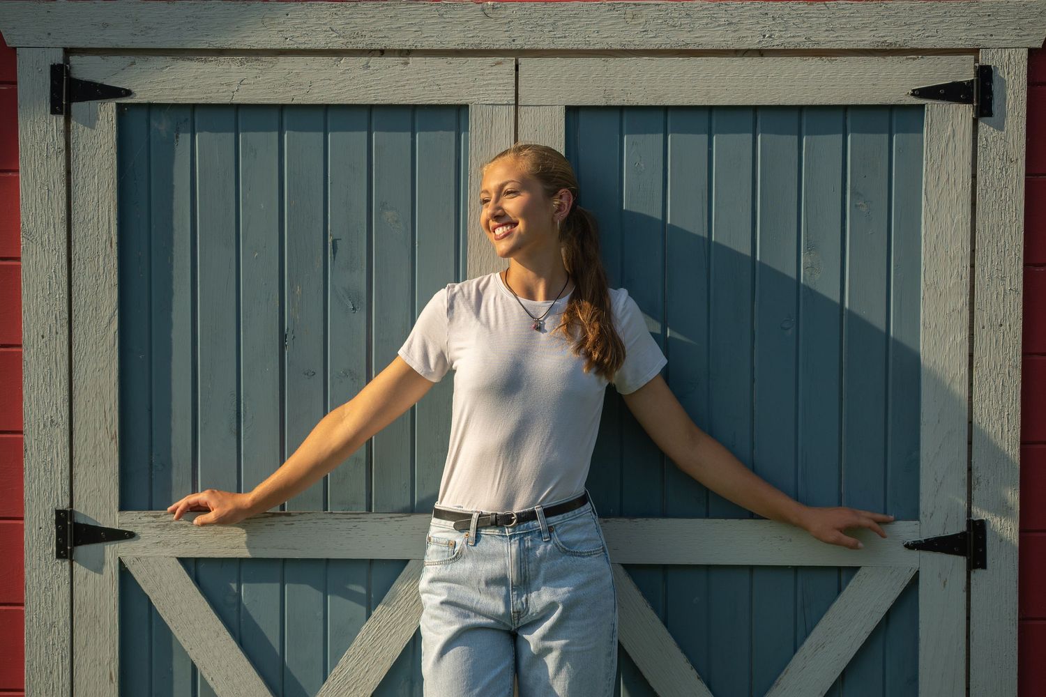 Person posing against blue barn doors in natural lighting.