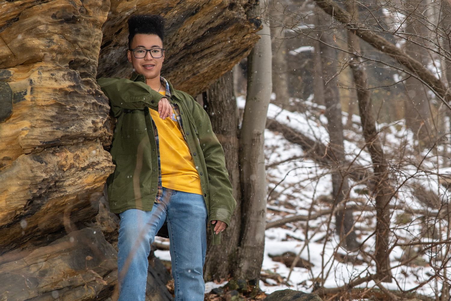 Someone in casual attire exploring a rocky winter landscape with snow-covered ground.