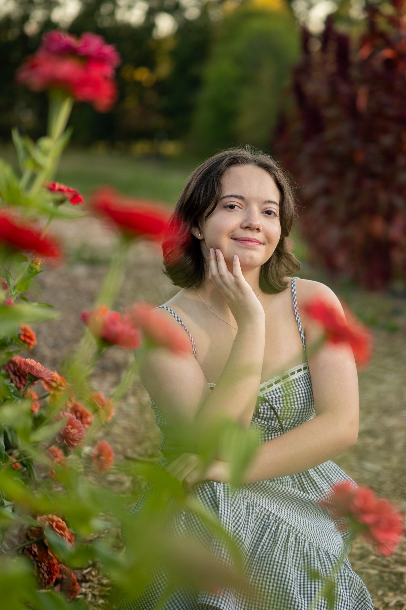 Person in gingham dress posing among garden flowers.