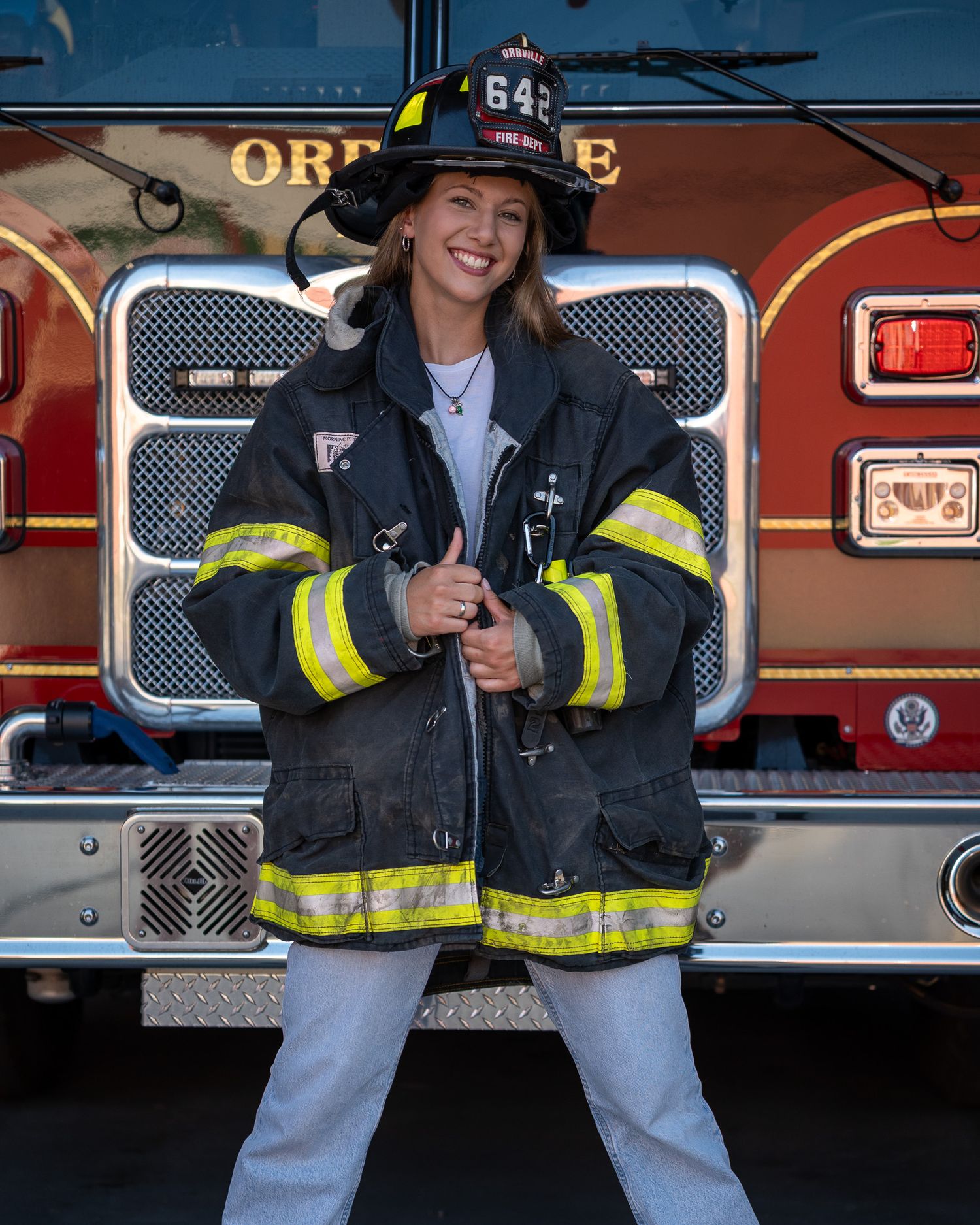 Wearing firefighter gear while posing next to red fire engine.