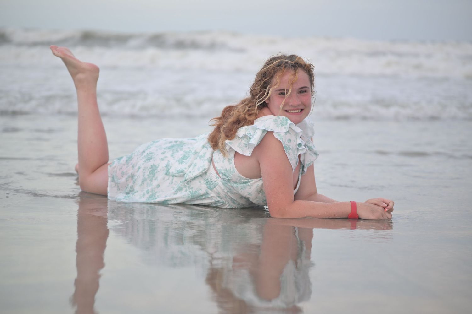 Person in a floral dress playing in ocean waves at the beach during overcast weather.