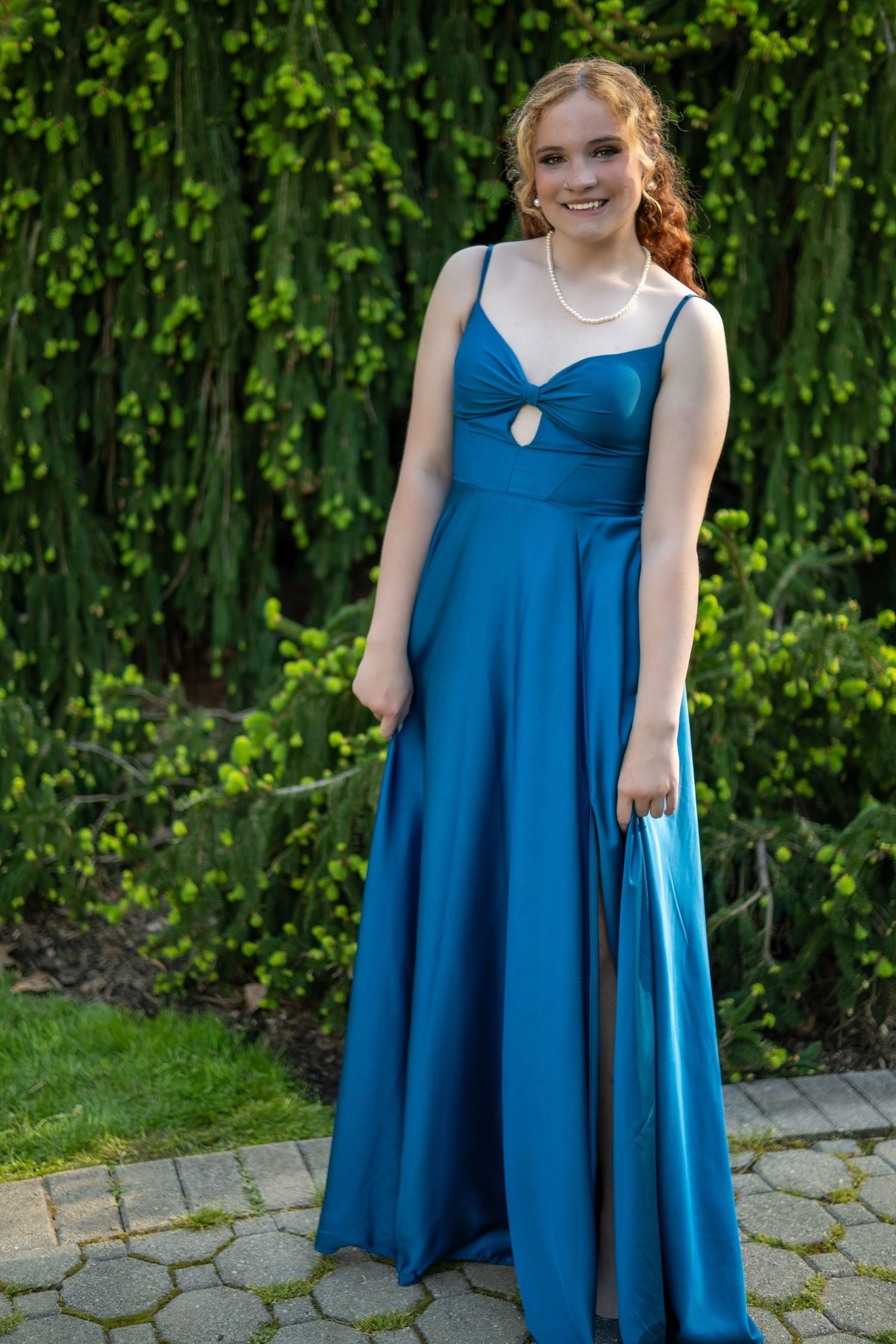A formal blue floor-length gown with a sweetheart neckline and keyhole detail against a green ivy backdrop.